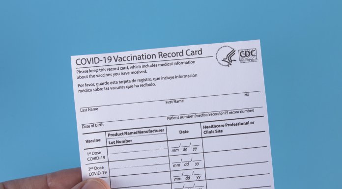 Hand holding a COVID-19 vaccination record card against a blue background