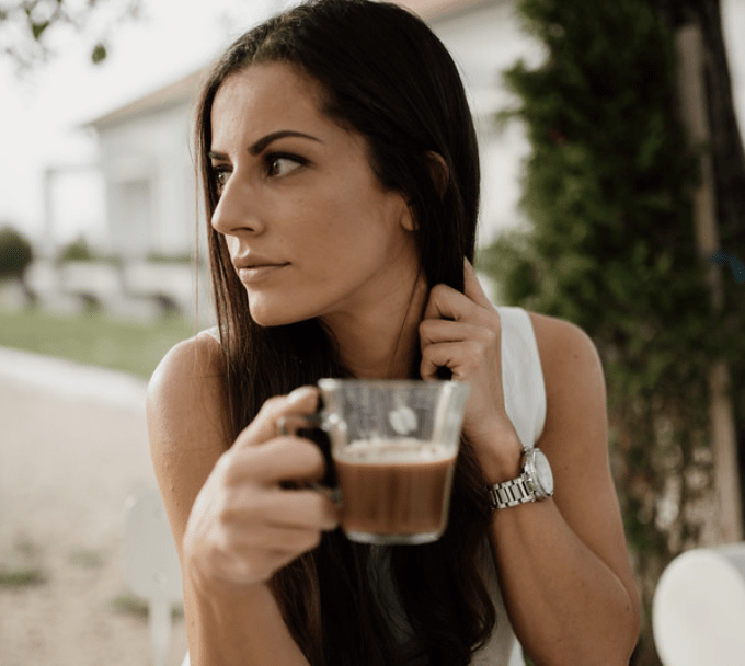 Woman sitting at the table and drinking coffee from a glass cup.