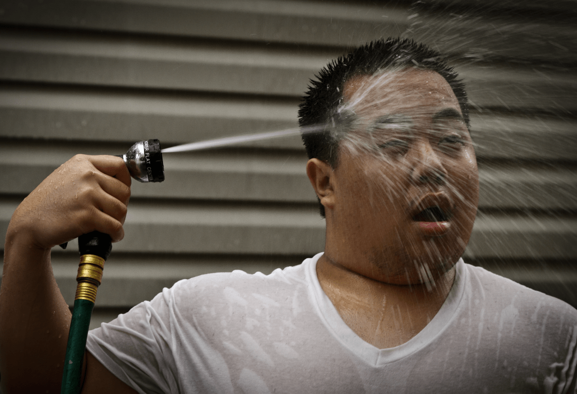A man seeks relief during a heat wave with a garden hose shower