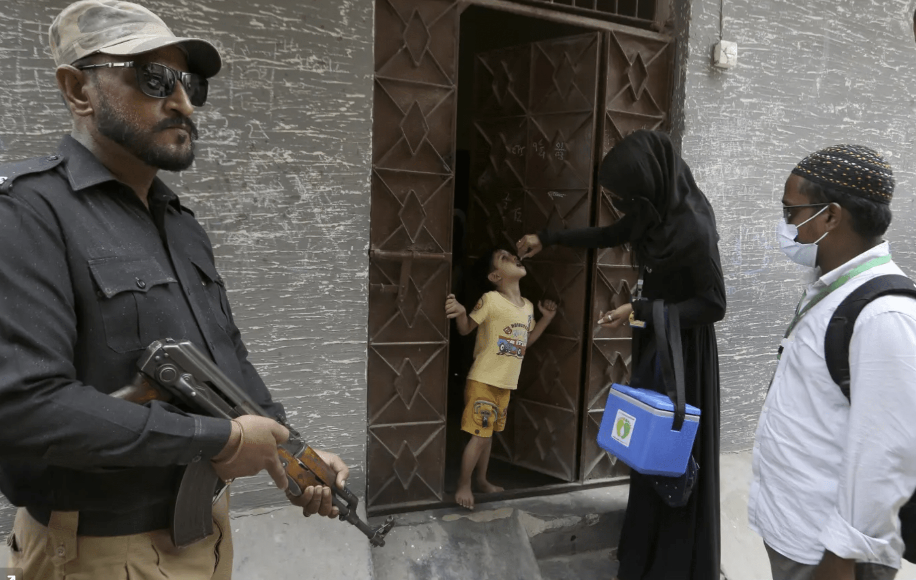 A police officer stands guard while a health-care worker administers a polio vaccine to a child in Karachi, Pakistan.