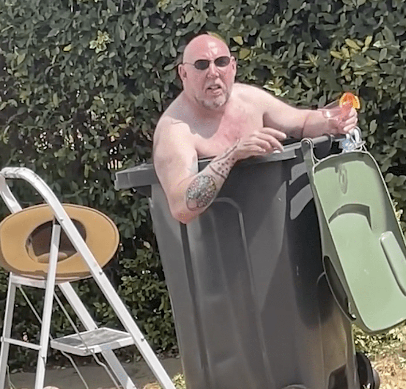 Bloke with a cocktail cools off in a trash barrel